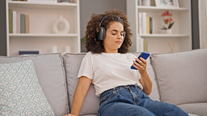 Young beautiful hispanic woman listening to music relaxed on sofa at home