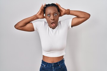Beautiful black woman standing over isolated background crazy and scared with hands on head, afraid and surprised of shock with open mouth