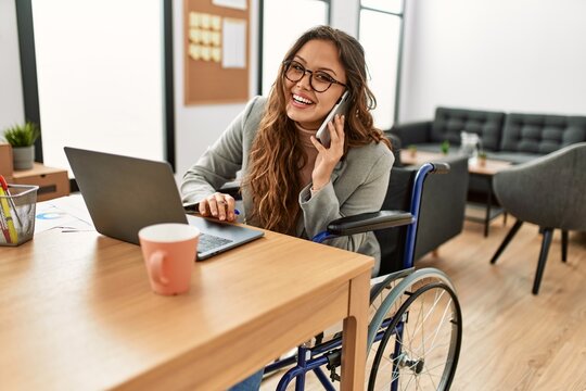 Young beautiful hispanic woman business worker talking on smartphone sitting on wheelchair at office