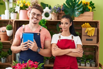 Man and woman florists using touchpad standing with arms crossed gesture at flower shop
