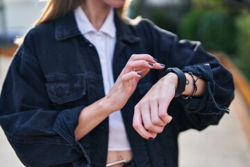 Young blonde woman touching watch at park