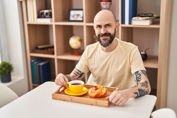 Young bald man having breakfast sitting on table at home