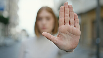 Young blonde woman doing stop gesture with hand at street