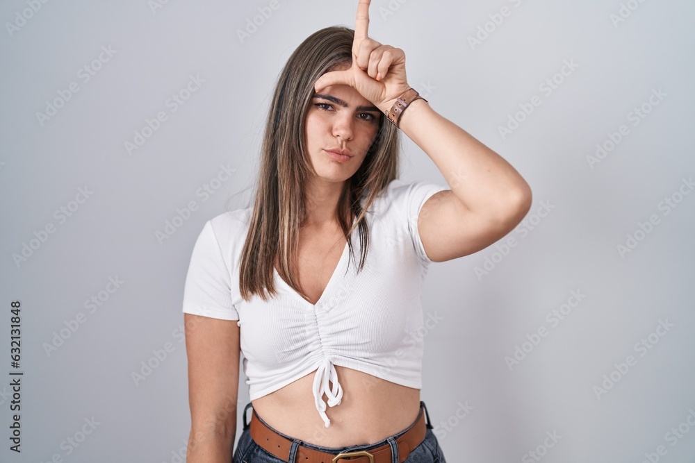 Sticker young beautiful woman wearing casual white t shirt making fun of people with fingers on forehead doi