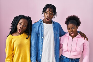 Group of three young black people standing together over pink background in shock face, looking skeptical and sarcastic, surprised with open mouth