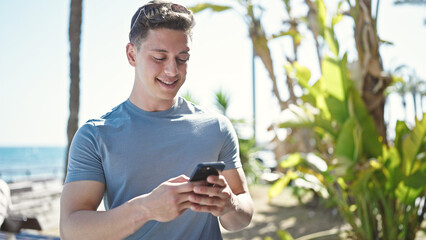 Young hispanic man tourist smiling confident using smartphone at seaside