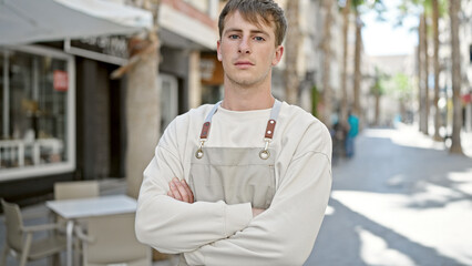 Young caucasian man waiter standing with arms crossed gesture and relaxed expression at coffee shop terrace