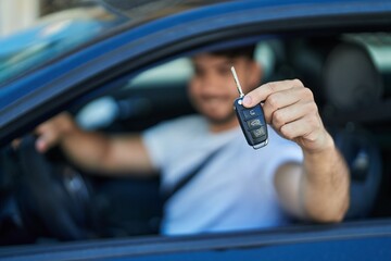 Young hispanic man smiling confident holding key of new car at street