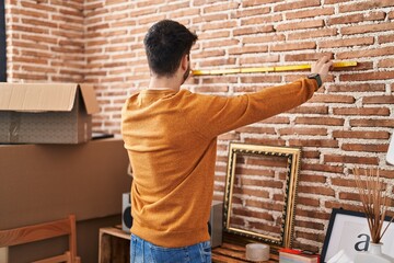 Young hispanic man measuring wall at new home