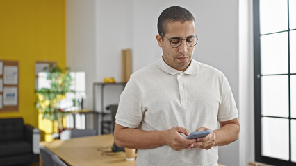 Naklejka na ściany i meble Young hispanic man business worker using smartphone at office