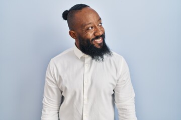 African american man standing over blue background looking away to side with smile on face, natural expression. laughing confident.