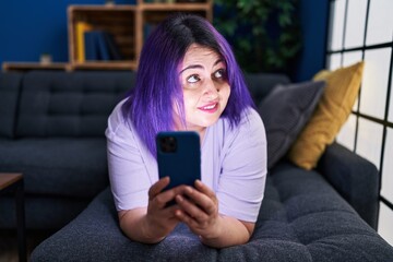 Young beautiful plus size woman using smartphone lying on sofa at home