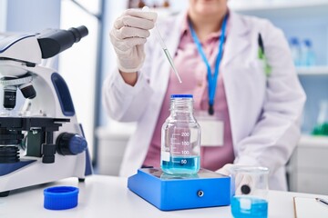 Young beautiful plus size woman scientist pouring liquid on test tube weighing liquid at laboratory