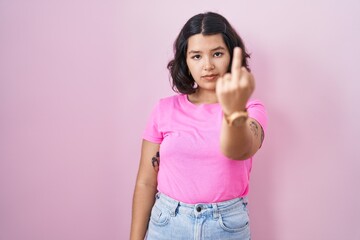 Young hispanic woman standing over pink background showing middle finger, impolite and rude fuck...