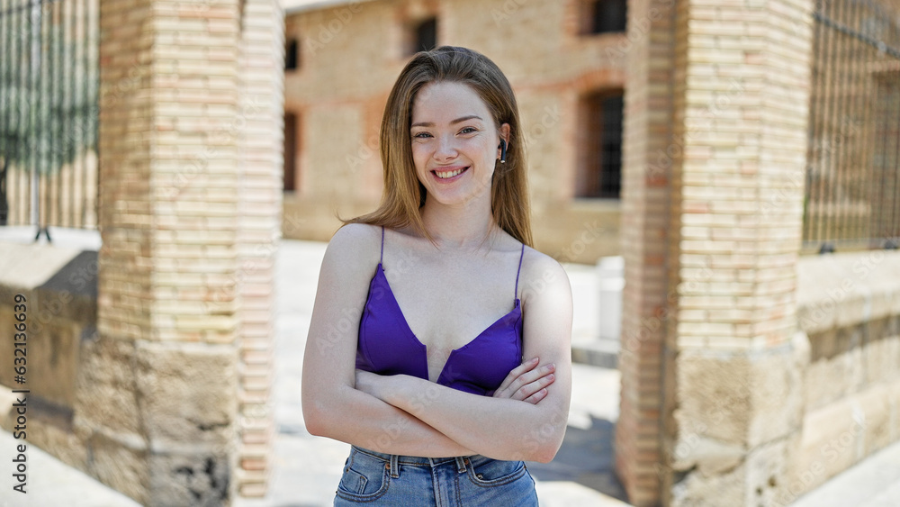 Sticker Young blonde woman wearing earphones standing with arms crossed gesture smiling at street