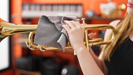Young blonde woman musician cleaning trumpet at music studio