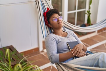 African american woman lying on hammock sleeping at home terrace