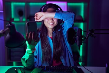 Young asian woman playing video games with smartphone smiling cheerful playing peek a boo with hands showing face. surprised and exited