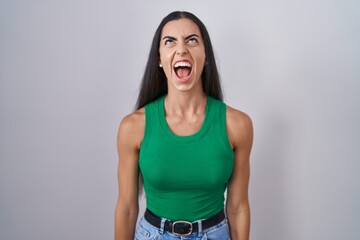 Young woman standing over isolated background angry and mad screaming frustrated and furious,...