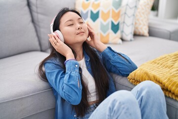 Fototapeta premium Young chinese woman listening to music sitting on floor at home