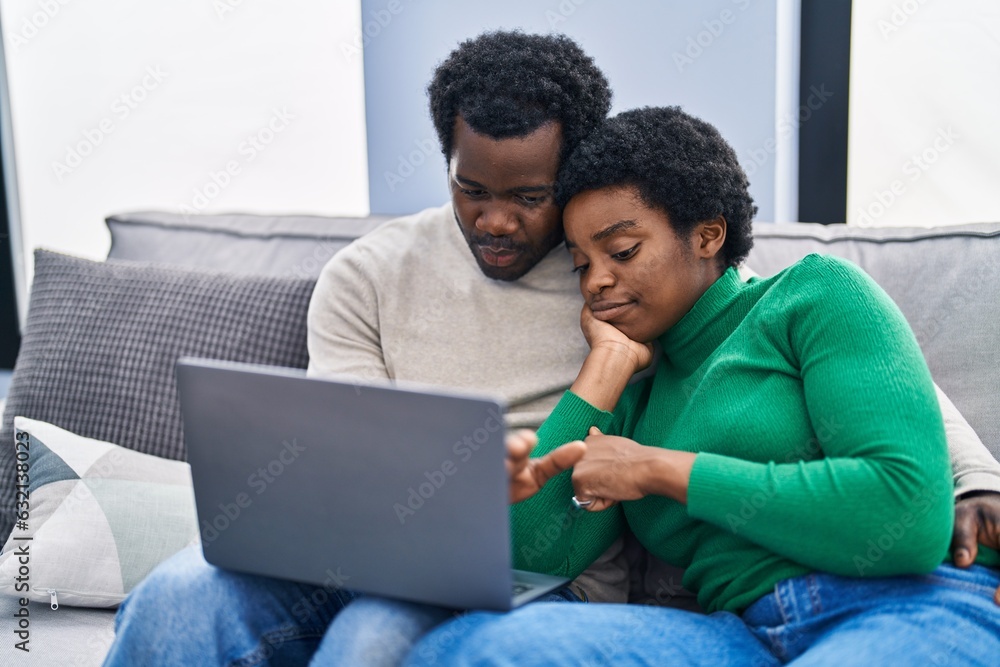 Poster african american man and woman couple using laptop sitting on sofa at home