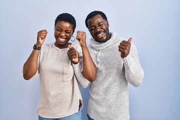 Young african american couple standing over blue background together excited for success with arms raised and eyes closed celebrating victory smiling. winner concept. - Powered by Adobe