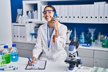 Young african american woman scientist talking on the smartphone write on report document at laboratory