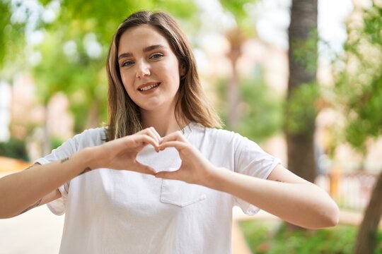 Young woman smiling confident doing heart gesture with hands at park