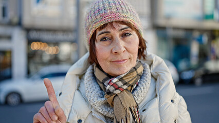 Mature hispanic woman standing with serious expression saying no with finger at street