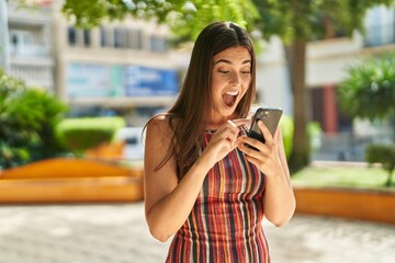 Young beautiful hispanic woman using smartphone with surprise expression at park