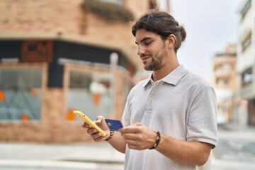 Young hispanic man using smartphone and credit card at street