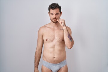 Young hispanic man standing shirtless wearing underware mouth and lips shut as zip with fingers....