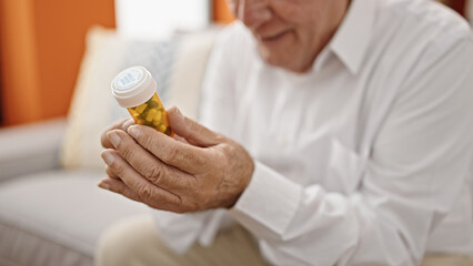 Senior grey-haired man holding pills bottle at home