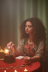 Serious fortune teller touching crystal ball in front of her