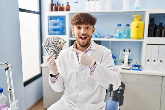 Arab man with beard working at scientist laboratory holding money smiling happy pointing with hand and finger