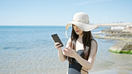 Young chinese woman tourist wearing swimsuit make selfie by smartphone at seaside