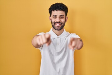 Arab man standing over yellow background pointing to you and the camera with fingers, smiling positive and cheerful