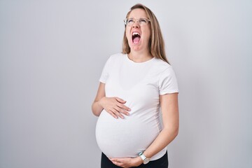 Young pregnant woman expecting a baby, touching pregnant belly angry and mad screaming frustrated...