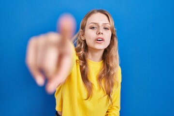 Young caucasian woman standing over blue background pointing displeased and frustrated to the...