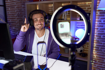 Hispanic man with beard playing video games recording with smartphone smiling with an idea or...