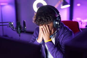 Young hispanic teenager streamer stressed using computer at gaming room