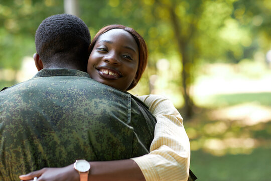 Happy African American woman embracing her military husband while they standing outdoors