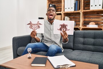 African american man working with rorschach test at psychology clinic angry and mad screaming...