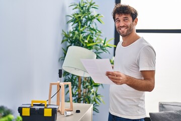Young man smiling confident repairing lamp reading instructions at home