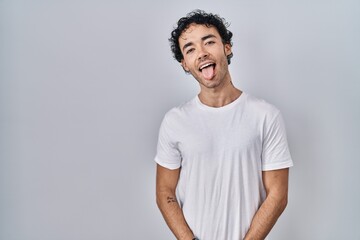 Hispanic man standing over isolated background sticking tongue out happy with funny expression. emotion concept.