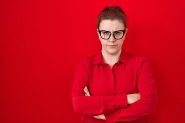 Young hispanic woman with red hair standing over red background skeptic and nervous, disapproving...