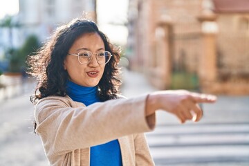 Young chinese woman smiling confident pointing with finger at street