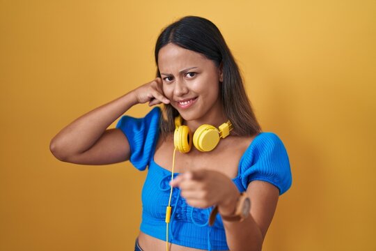 Hispanic young woman standing over yellow background smiling doing talking on the telephone gesture and pointing to you. call me.