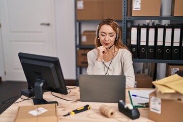 Hispanic woman working at small business ecommerce wearing headset serious face thinking about...