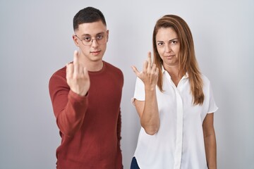Mother and son standing together over isolated background showing middle finger, impolite and rude...